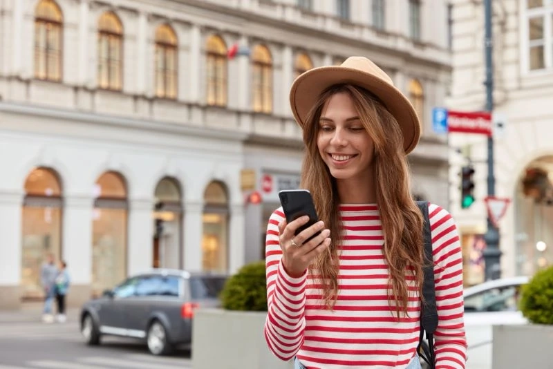 Uśmiechnięta dziewczyna sprawdza na telefonie oferty pożyczki przez SMS